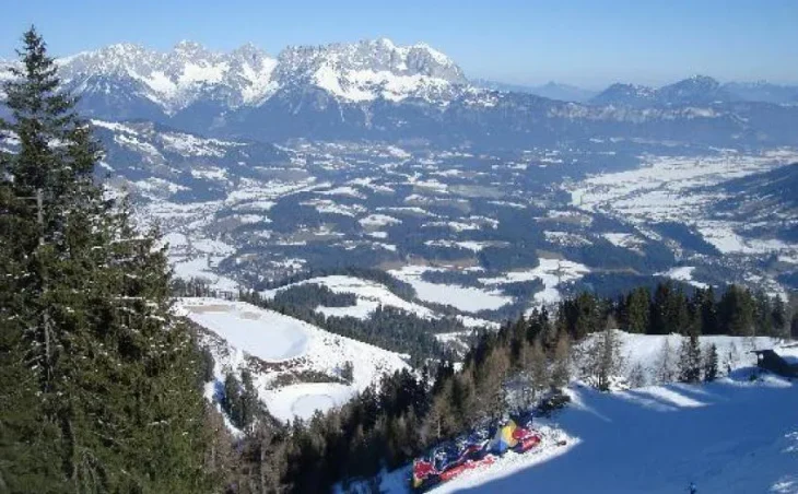 A view across a snowy valley, lined with trees. In the distant the ski resort of Kitzbuhel can be seen