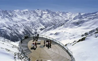 Figures stand on a viewing platform, high in the Austrian Alps looking over the landscape of Solden ski resort.