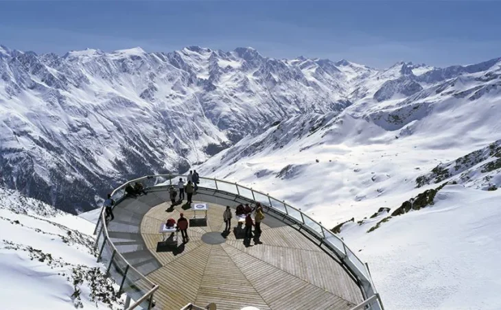 Figures stand on a viewing platform, high in the Austrian Alps looking over the landscape of Solden ski resort.