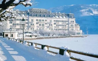 A snow covered white, palatial looking building in front of a frozen lake in Zell Am See, Austria