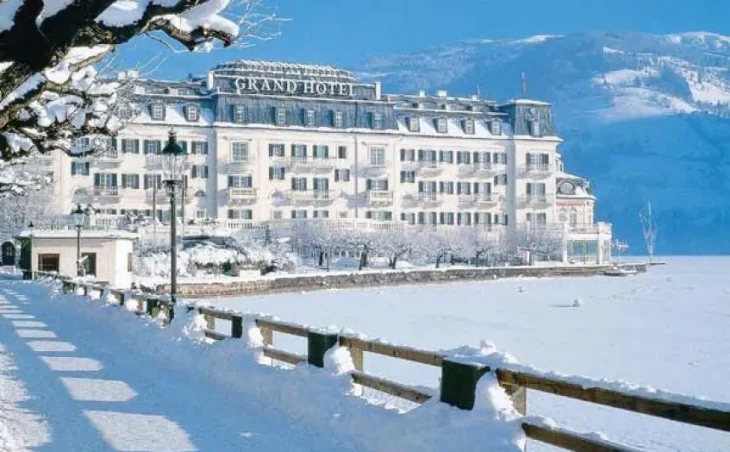 A snow covered white, palatial looking building in front of a frozen lake in Zell Am See, Austria
