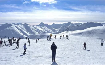 A sunny day at the Italian ski resort of Livigno. Skiers are on the piste and snowy mountain tops are in the distance
