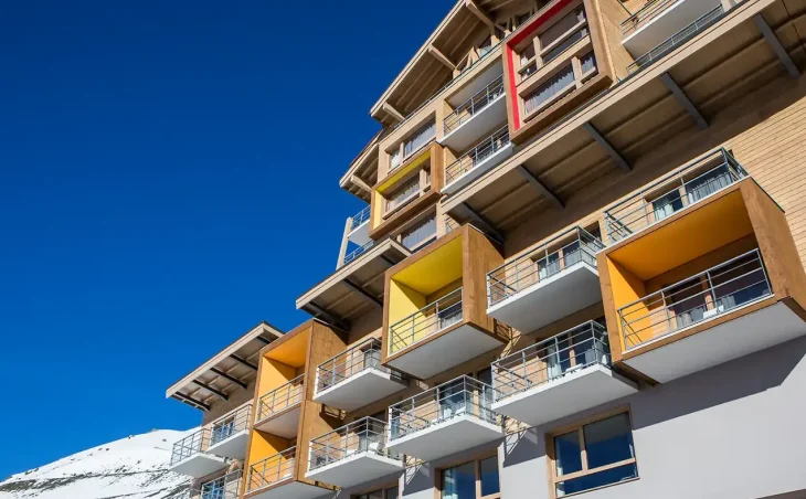 All-inclusive ski holidays in France. A picture of the outside of the Val Thorens Sensations all-inclusive hotel. Balconies are flooded in bright sunlight. A snowy mountain is in the background. 