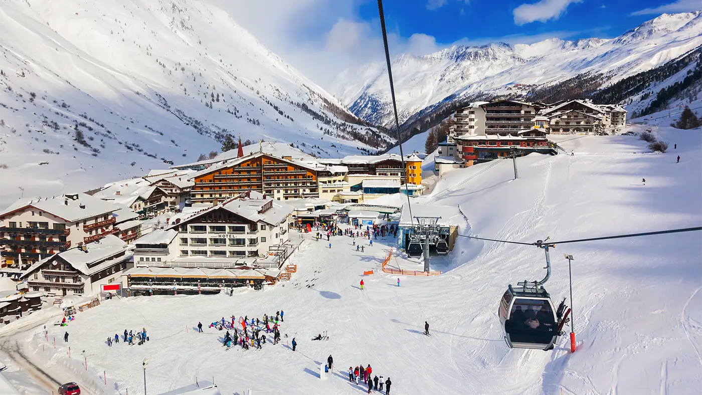 A photo of the ski resort of Obergurgl, taken from a cable car. Chalets, hotels and resort buildings can be seen from above with skiers gathered on the pistes.