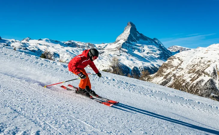 A young skier at speeding Zermatt, dressed in red, with the Matterhorn Mountain in the background i