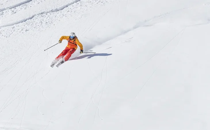 Downhill skier dressed in orange on a quiet piste on ski holiday in Italy