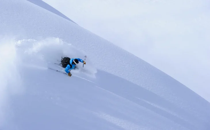 A skier in blue cuts through deep powder snow on a pristine snow covers slope on a ski holiday in Japan