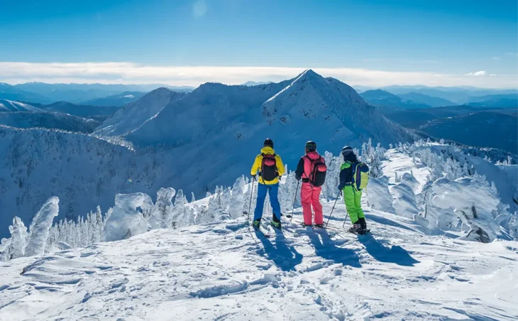 3 skiers stand at the peak of a mountain looking out at the vista of the Julian Alps on a ski holiday in Slovenia