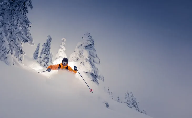 A skier in orange enjoys skiing through deep powder snow on a ski holiday in Spain