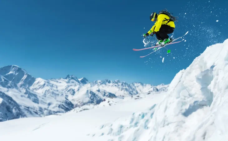 A skier in a yellow and black outfit jumps off performs a ski jump on a ski holiday in Switzerland