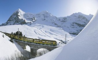 A mountain train crosses a bridge between 2 snow-covered mountains in Grindelwald, Switzerland.