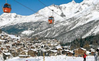 Red cable cars above skiers on the pistes in Saas Fee, Switzerland.